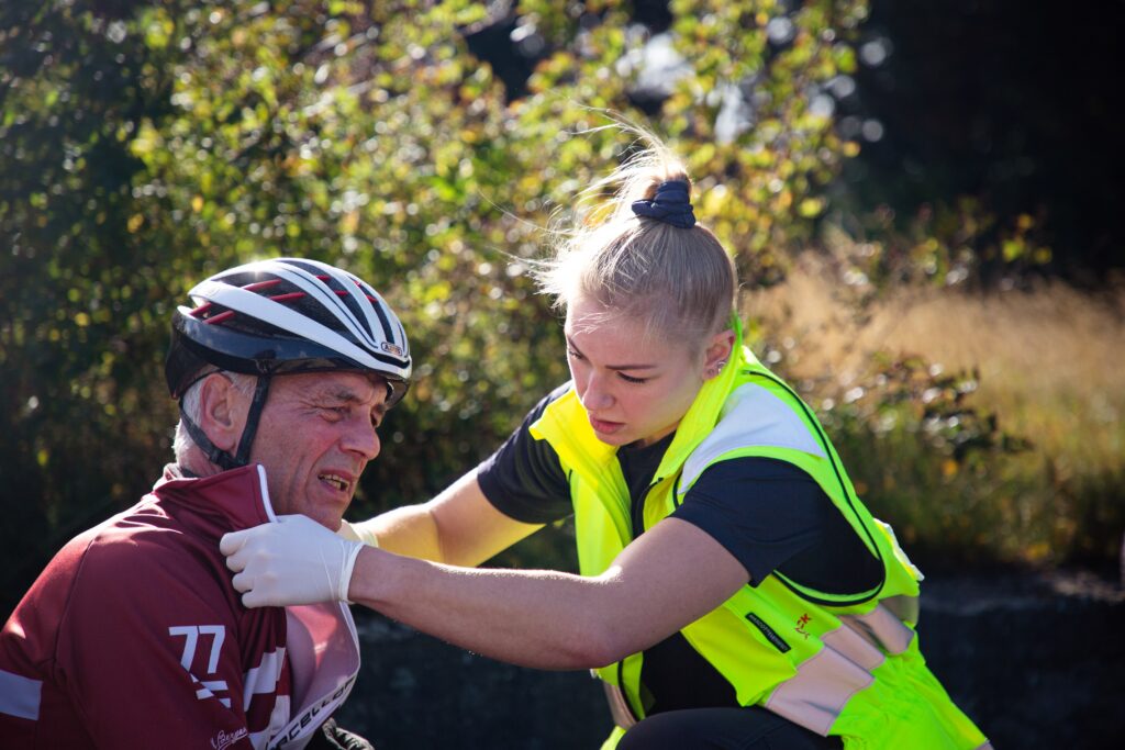 Ung ambulancebehandler undersøger og beroliger tilskadekommen cyklist med cykelhjelm på vejen.