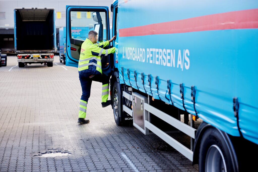 Godschauffør stiger ind i førerhuset på sin blå Nørgaard Petersen Scania-lastbil ved terminalen.
