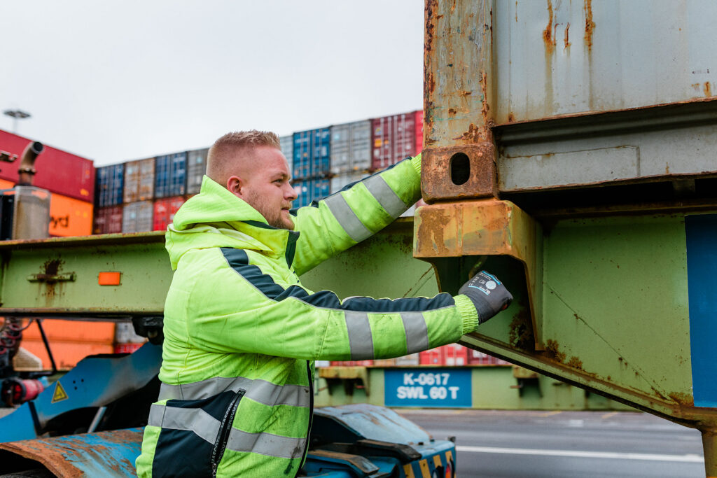 Terminalarbejder klargør containerlås og tjekker fastgøring på trailer med stak af containere bag.