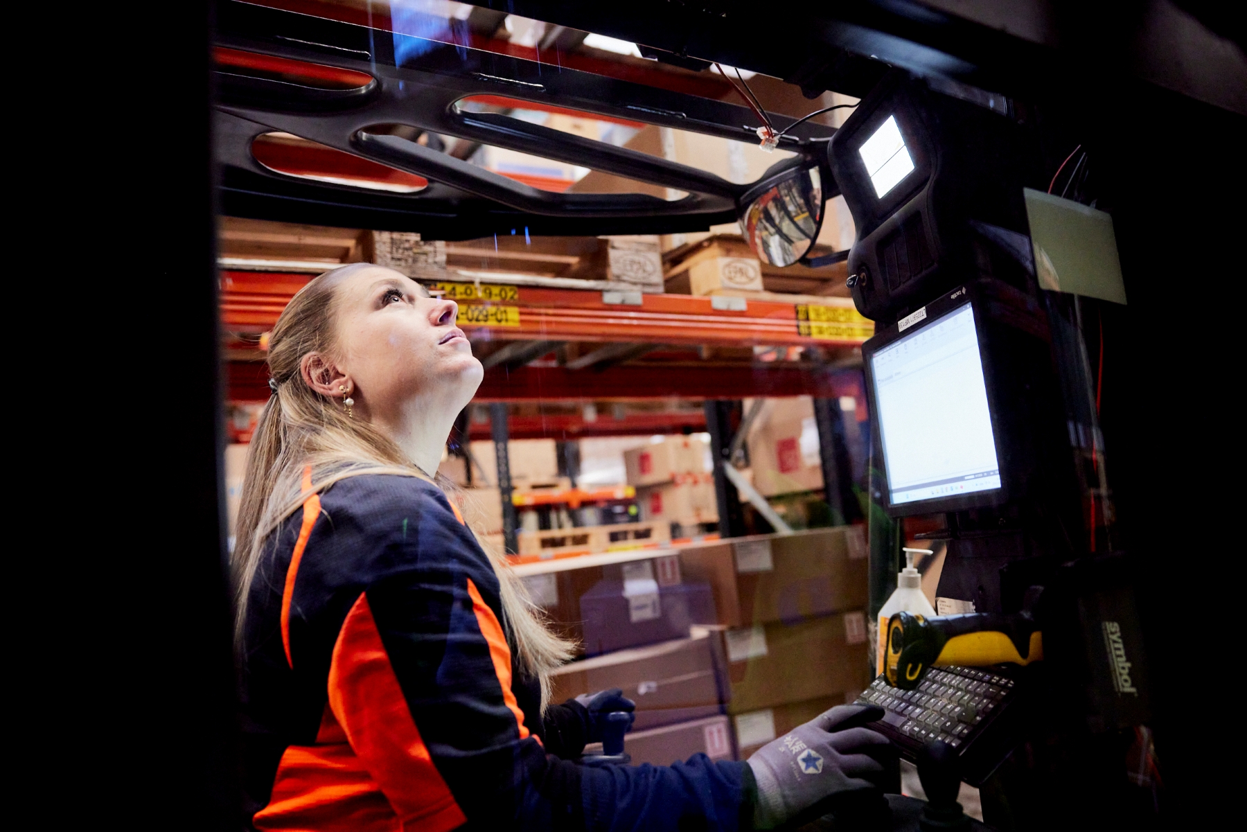 Truckfører i refleksjakke betjener gaffeltruck indefra førerkabinen.