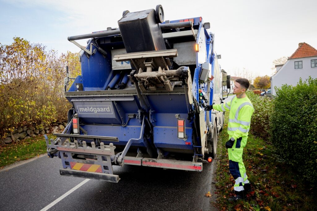 Renovationsmedarbejder betjener tømmesystemet bag på renovationsbilen ude på ruten.