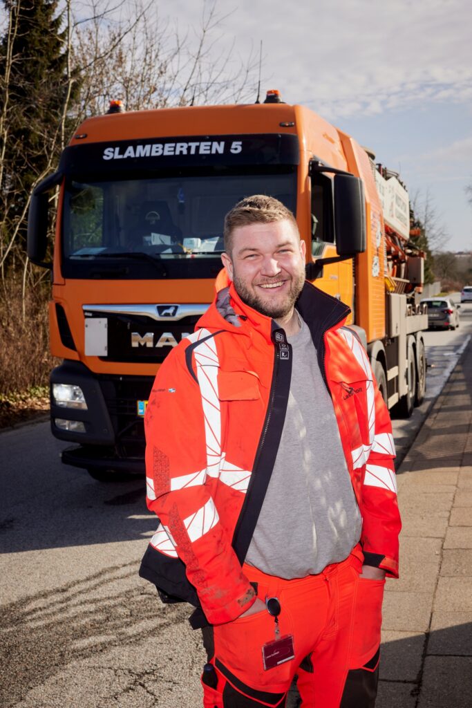 Portræt af kloakservice-chauffør foran MAN-lastbil på landevejen.